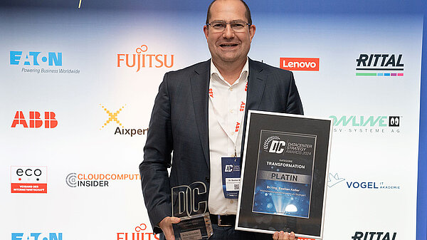 Photo of Bastian Koller holding awards in front of a logo wall.